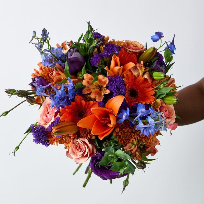 Bouquet of colorful flowers held by a person against a light gray background