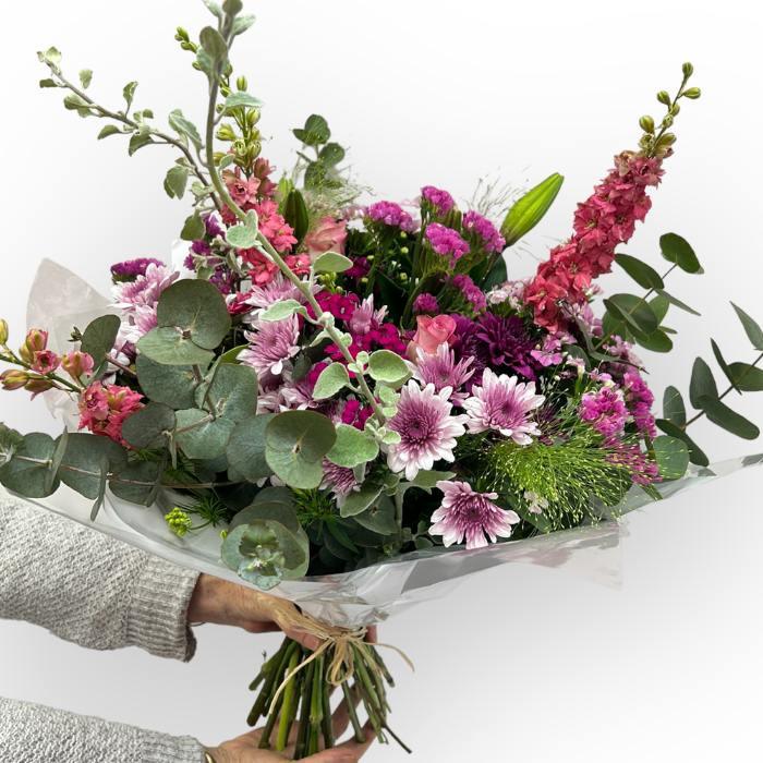 Bouquet of flowers with pink and purple flowers and green leaves, held by a person.