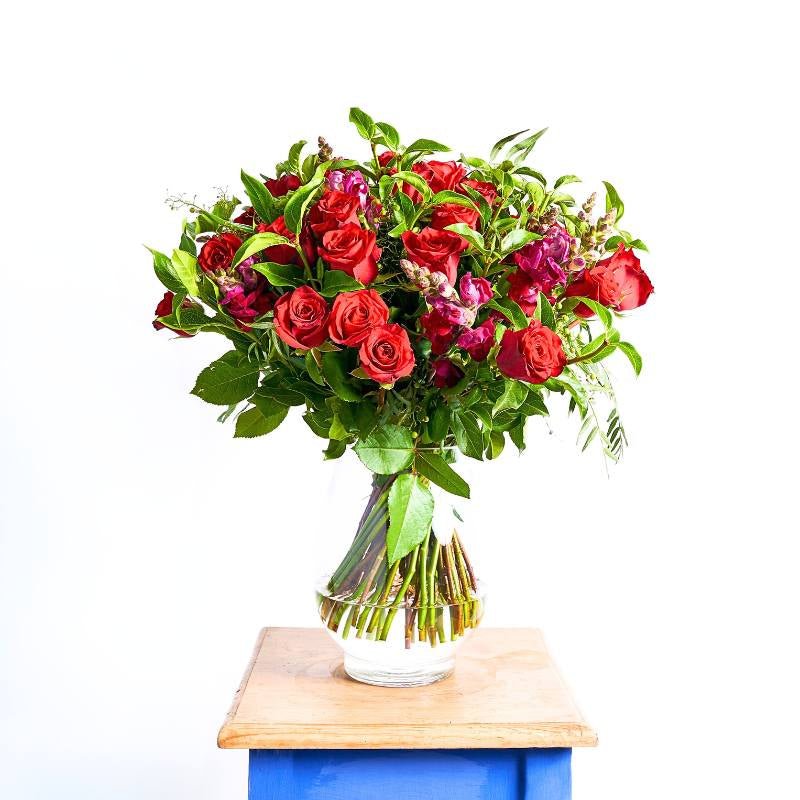 Arrangement of red and pink roses with green leaves in a clear vase on a white background