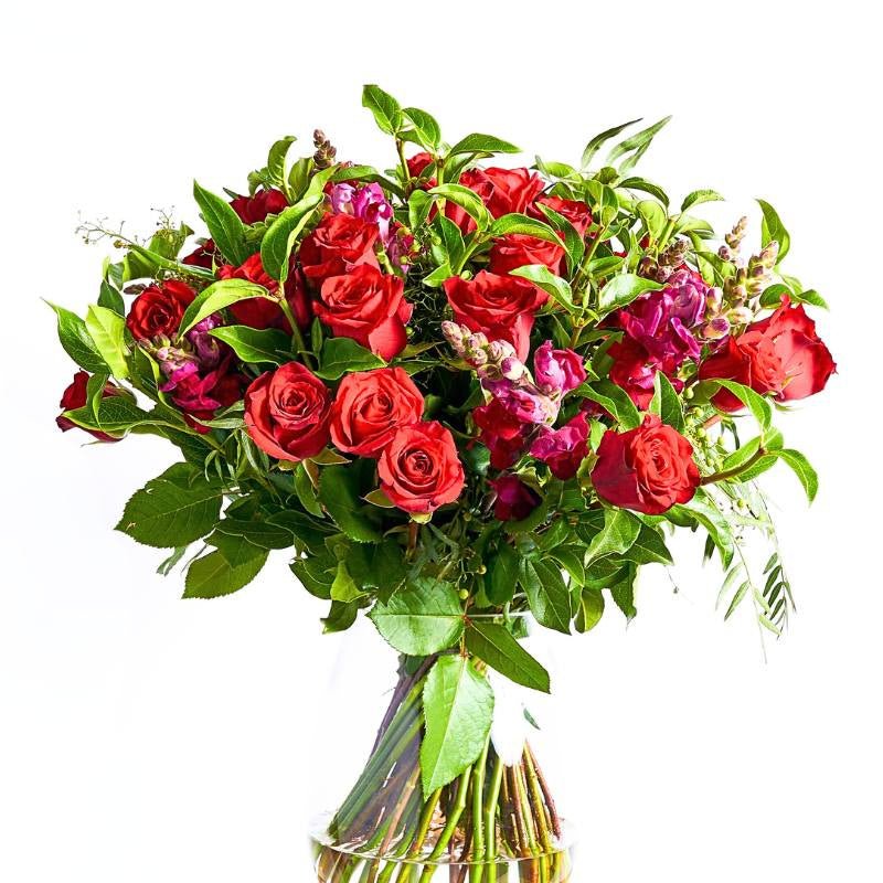 Arrangement of red and pink roses with green leaves in a clear vase on a white background