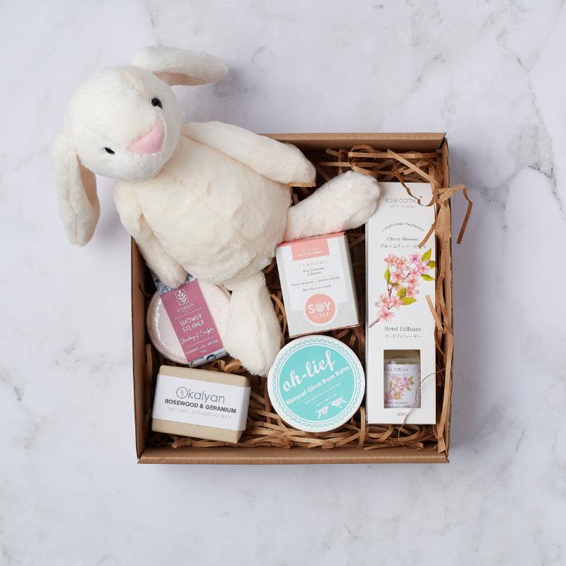 Pamper Bunny for Baby Girl gift box featuring a soft bunny toy, olive bum balm, cherry blossom reed diffuser, soap bar, and shower steamer.