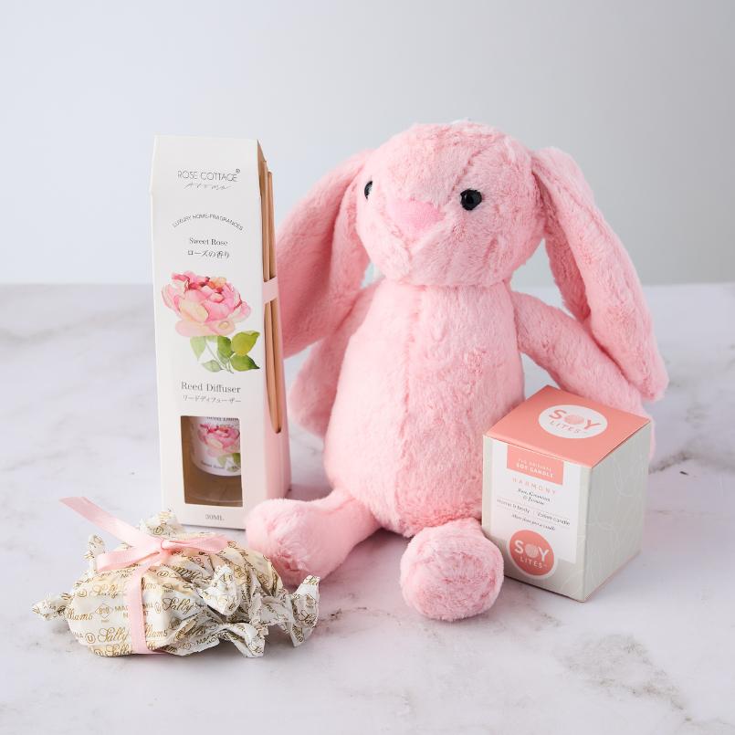 Pamper Bunny Gift Set featuring a plush pink bunny, Rose Cottage reed diffuser, Soy Lites candle, and Sally Williams nougat, beautifully arranged on a white surface.
