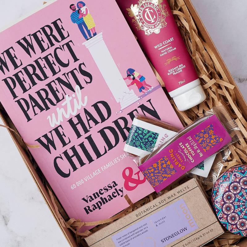 Close-up of the Parent's Pause Gift Box featuring the book 'We Were Perfect Parents Until We Had Children,' hand cream, chocolate, and soy wax melts.