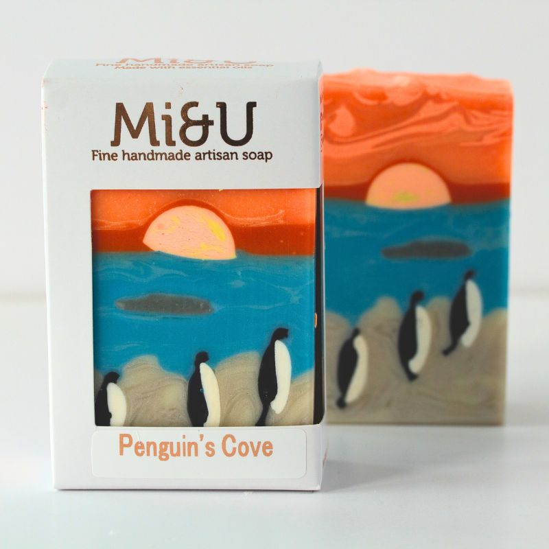 Soap bar with 'Penguin's Cove' design and packaging labeled 'Mi&U' on a light background