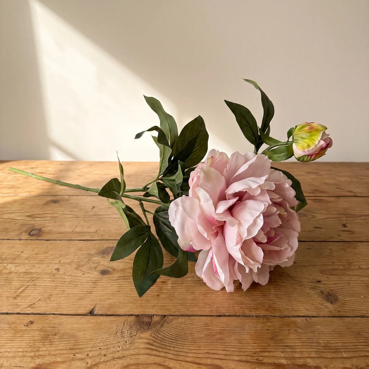 Mauve peony artificial flower, a single silk stem with bud lying on a wooden table