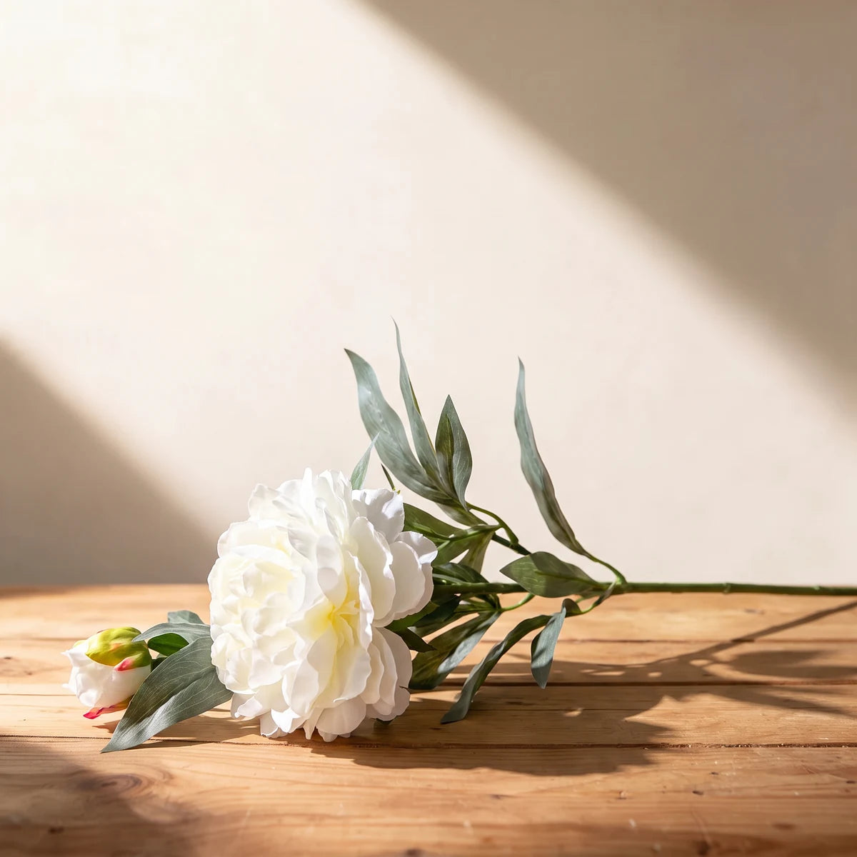 White peony artificial flower, a single silk stem with bud lying on a wooden table