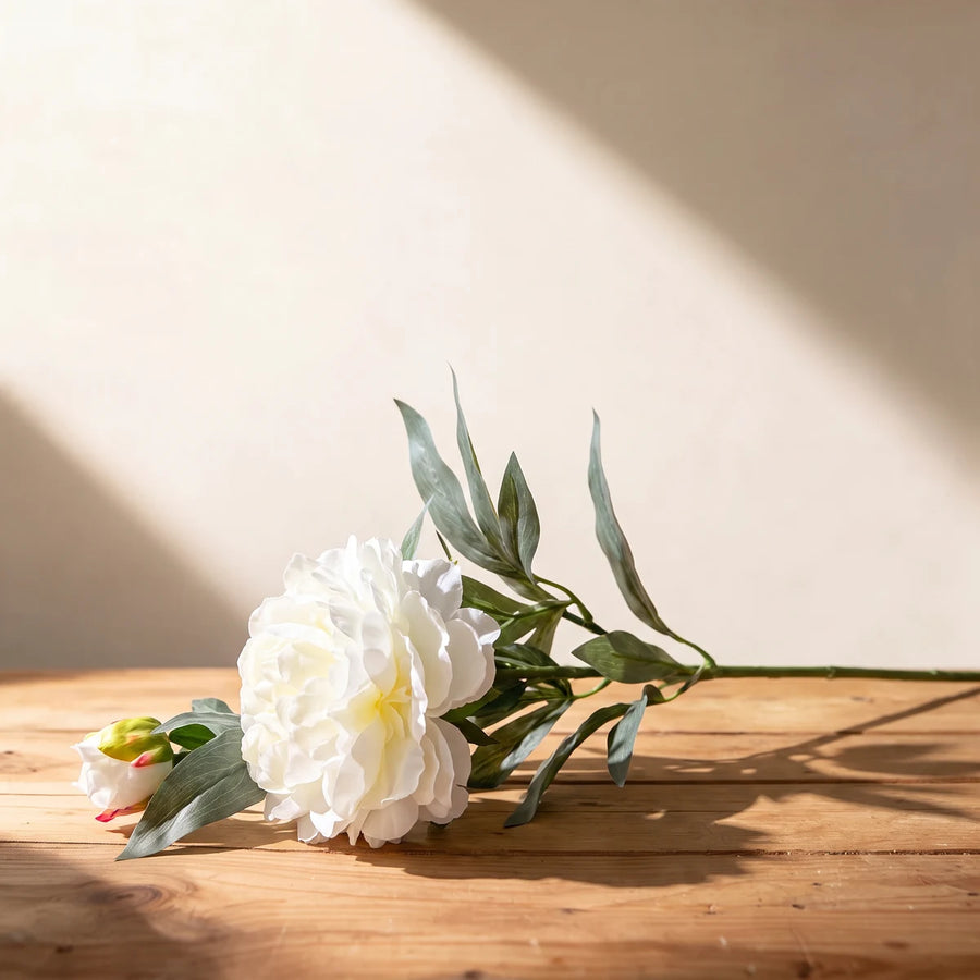 White peony artificial flower, a single silk stem with bud lying on a wooden table