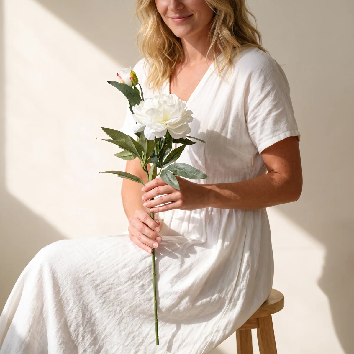 Woman seated with a single white silk peony stem, a long-lasting flower gift