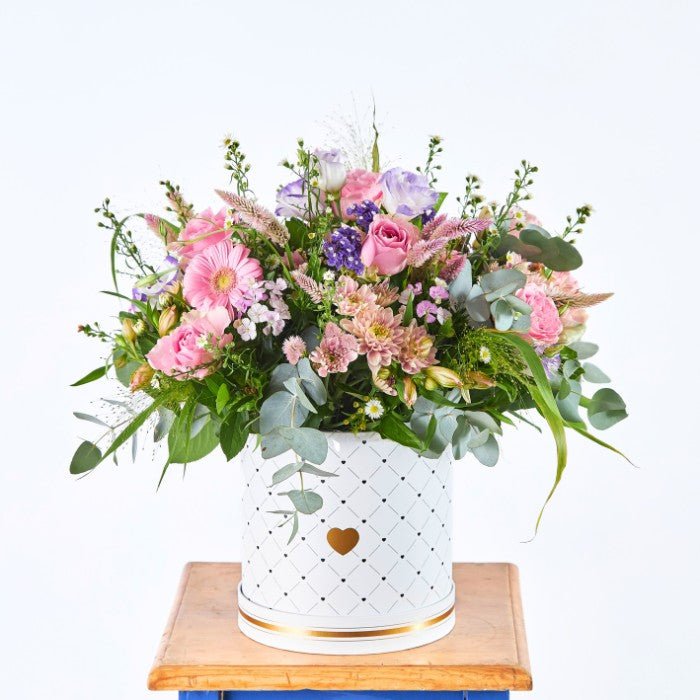 Overhead view of a lush flower arrangement with a mix of pink roses, purple lisianthus, gerberas, and assorted wildflowers in a full, vibrant display.