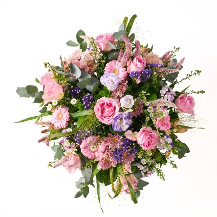 Side view of a charming flower arrangement in a white, heart-accented container, featuring pink roses, gerberas, and mixed blooms in soft pastels.