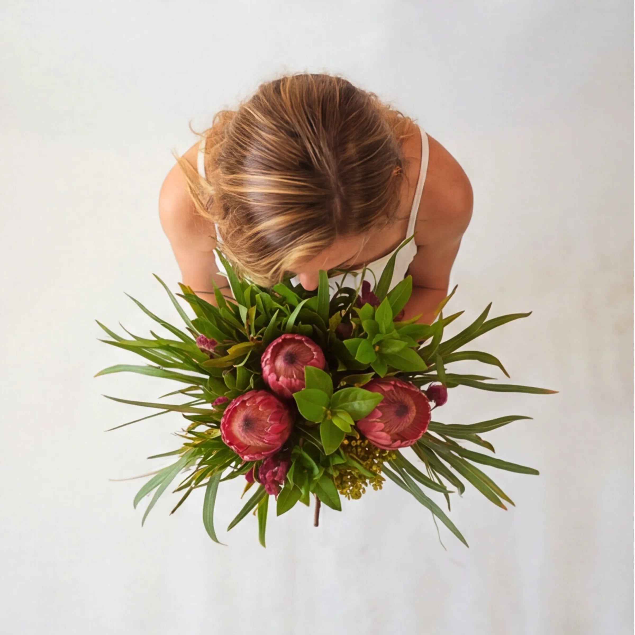 Top-down view of Protea Garden Flower Bouquet showing three pink king proteas, strappy eucalyptus, magenta celosia, yellow solidago and lush salal foliage hand-tied in a fynbos garden-style arrangement, locally grown by Fabulous Flowers South Africa