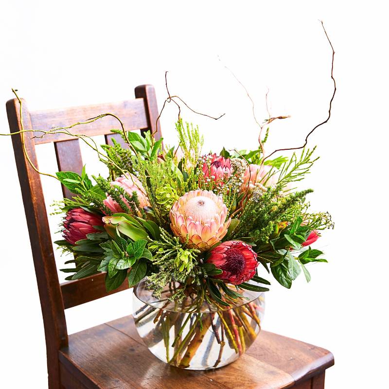 Arrangement of flowers in a clear vase on a wooden chair with a white background