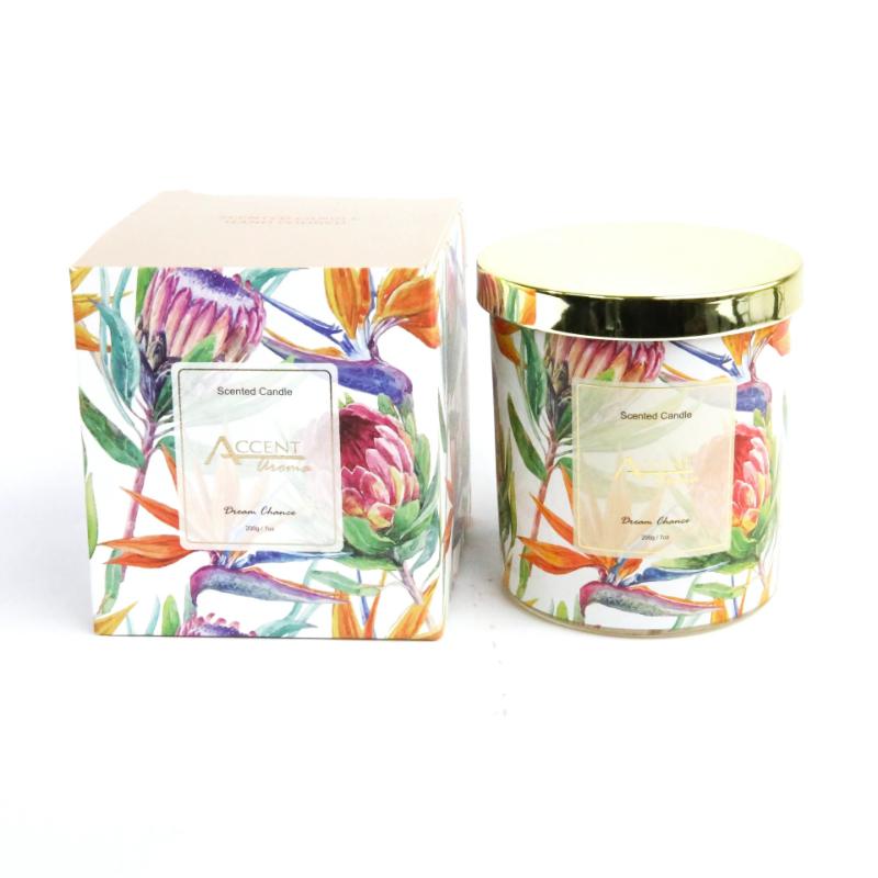 Decorative candle with protea floral design and matching packaging on a white background