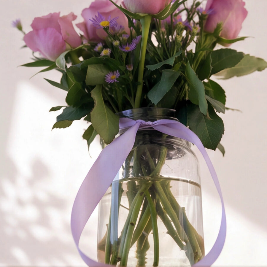 Glass vase of the Provence arrangement with lavender rose stems in water, tied with a lilac satin ribbon