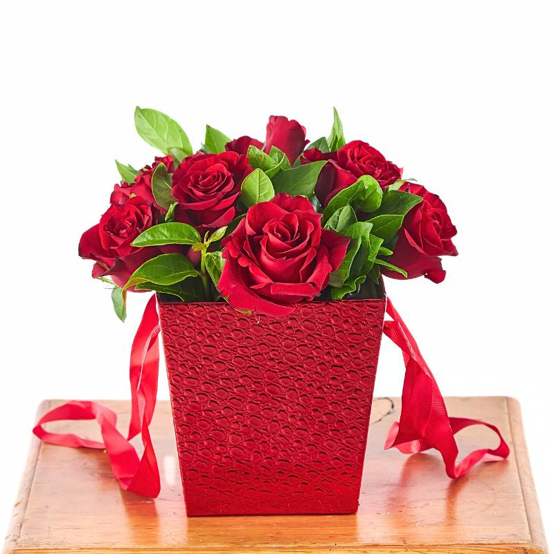 Bouquet of red roses in a red box with ribbons on a wooden surface