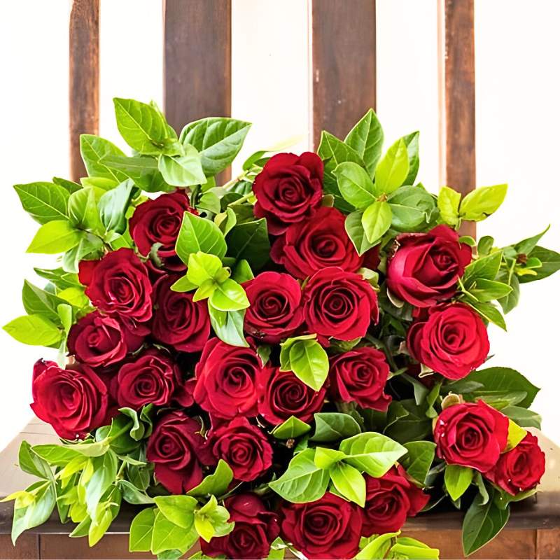 Bouquet of red roses with green leaves on a wooden surface