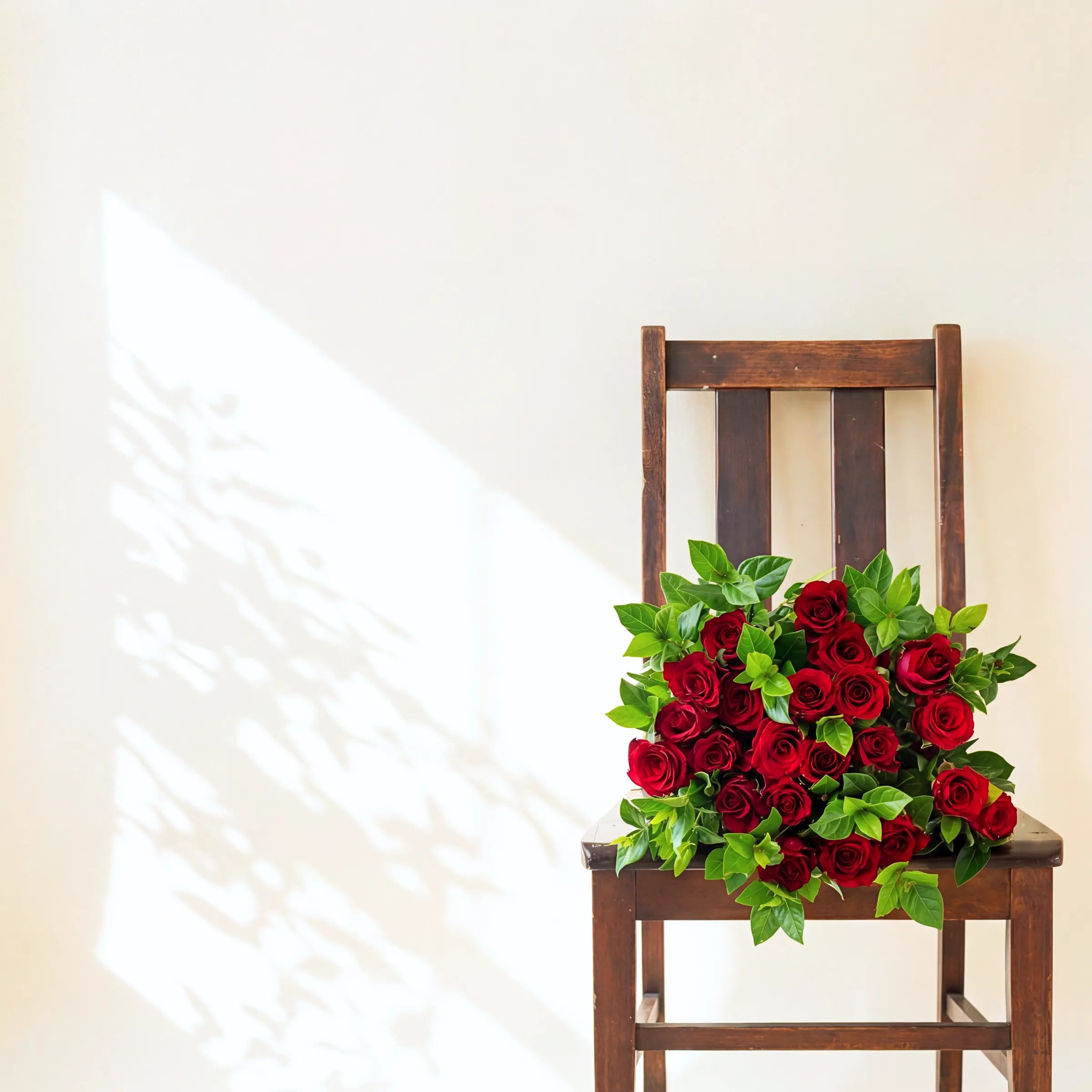 Red rose bouquet with fresh green foliage on a wooden chair in soft light, hand-tied by Fabulous Flowers Cape Town