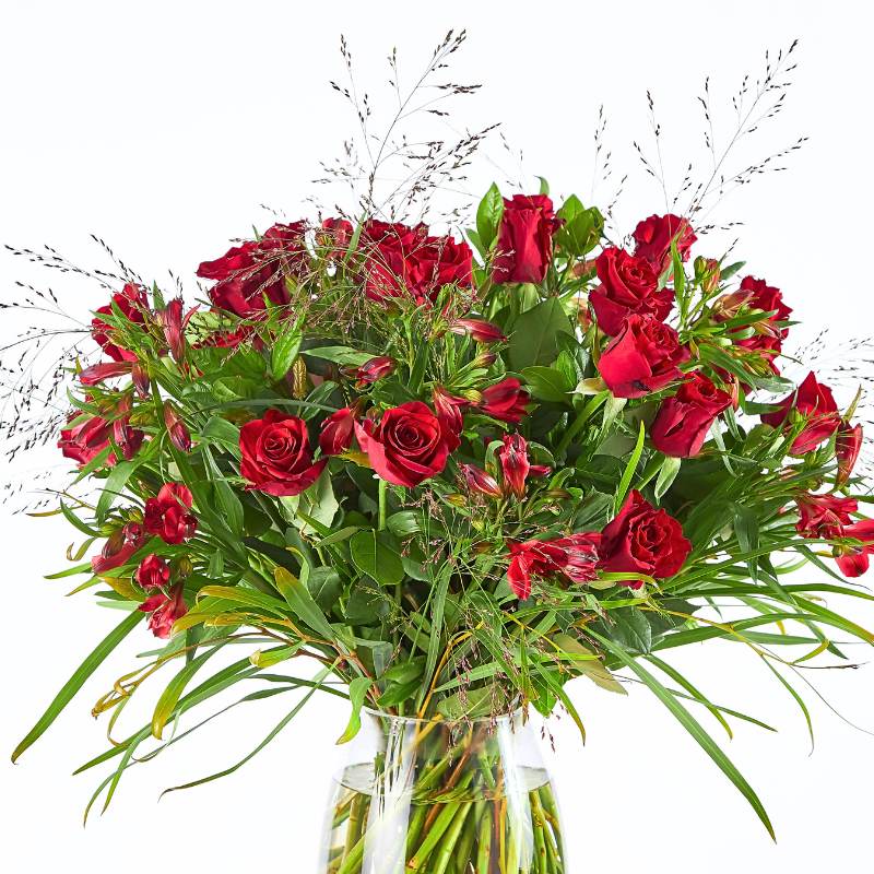 Flower arrangement of red roses with greenery in a clear vase on a white background