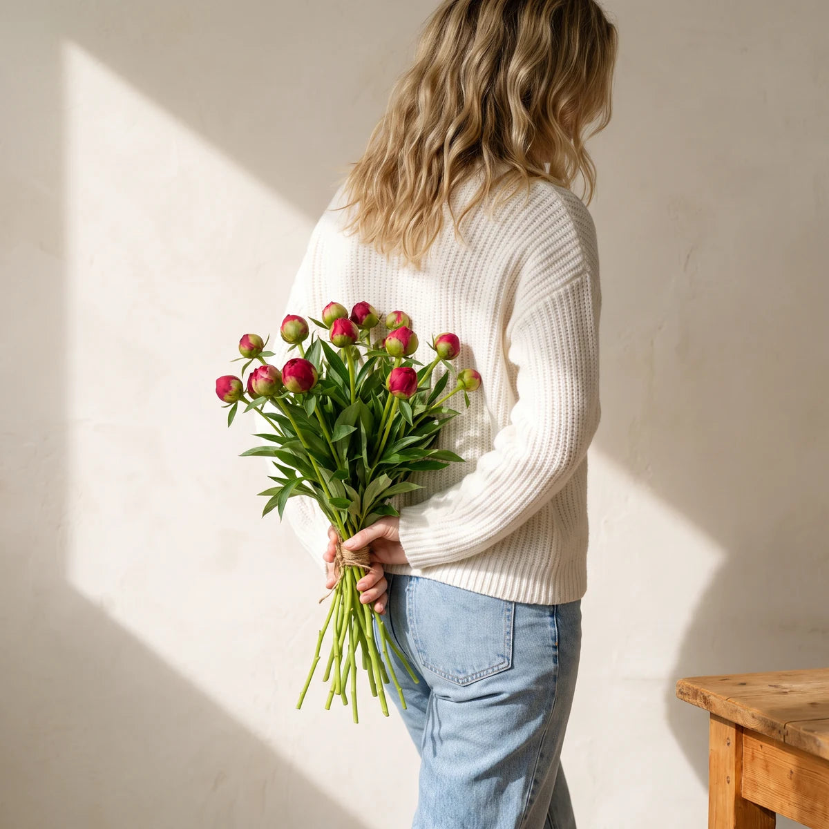Blonde woman walking with red peonies held behind her back as a surprise gift