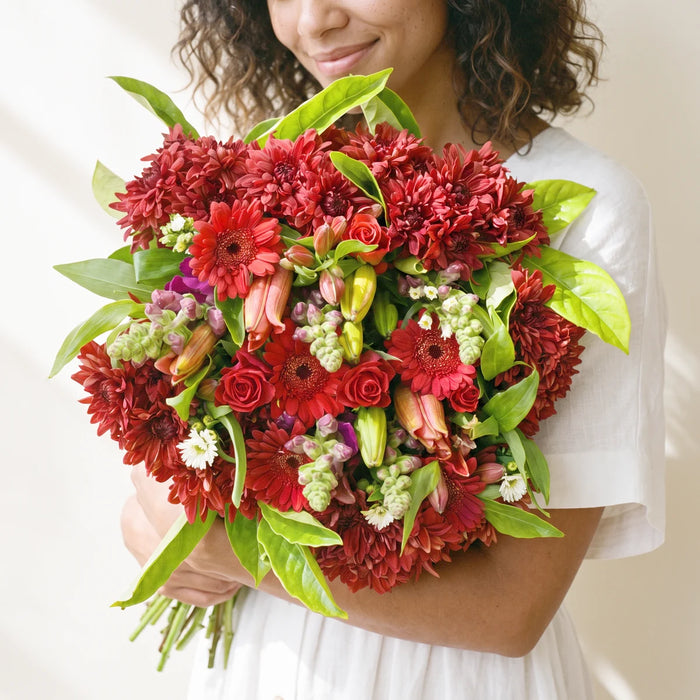 Smiling woman in a white linen dress hugging a large mixed red flower bouquet to her chest, Fabulous Flowers South Africa
