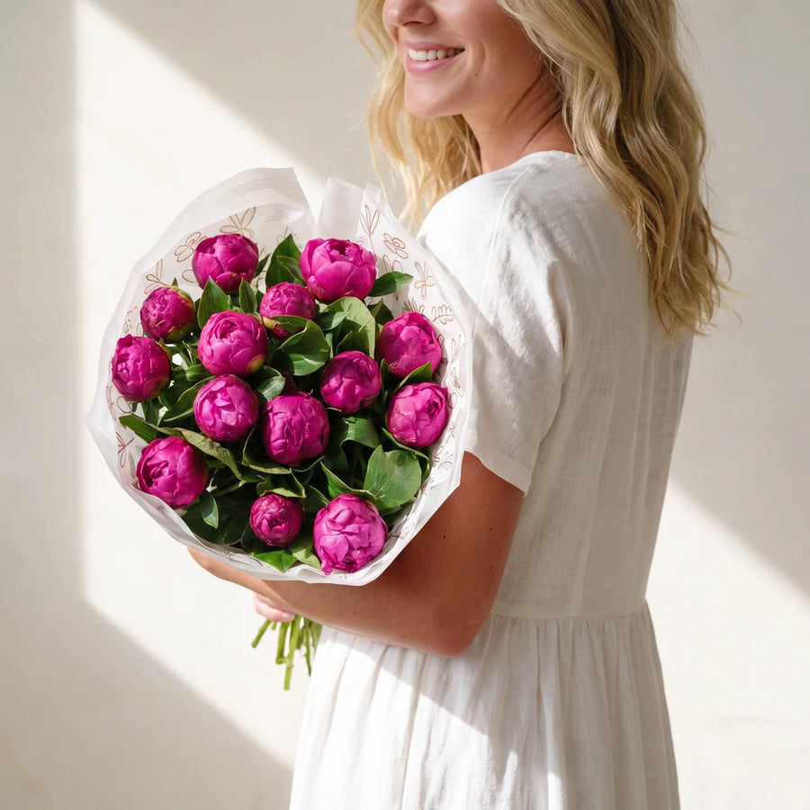 Blonde woman in a white dress turned away from the camera with a large bouquet of magenta peonies resting on her shoulder, Fabulous Flowers South Africa