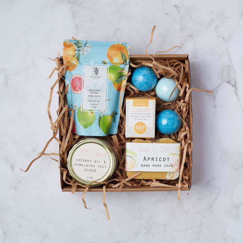Relax and Unwind Gift Box featuring grapefruit and lime bath salts, coconut oil salt scrub, apricot soap, blue bath bombs, and a soy candle.