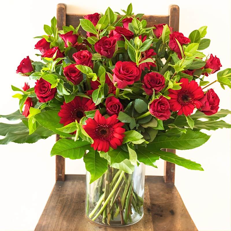 Large arrangement of red roses in a clear vase on a wooden chair
