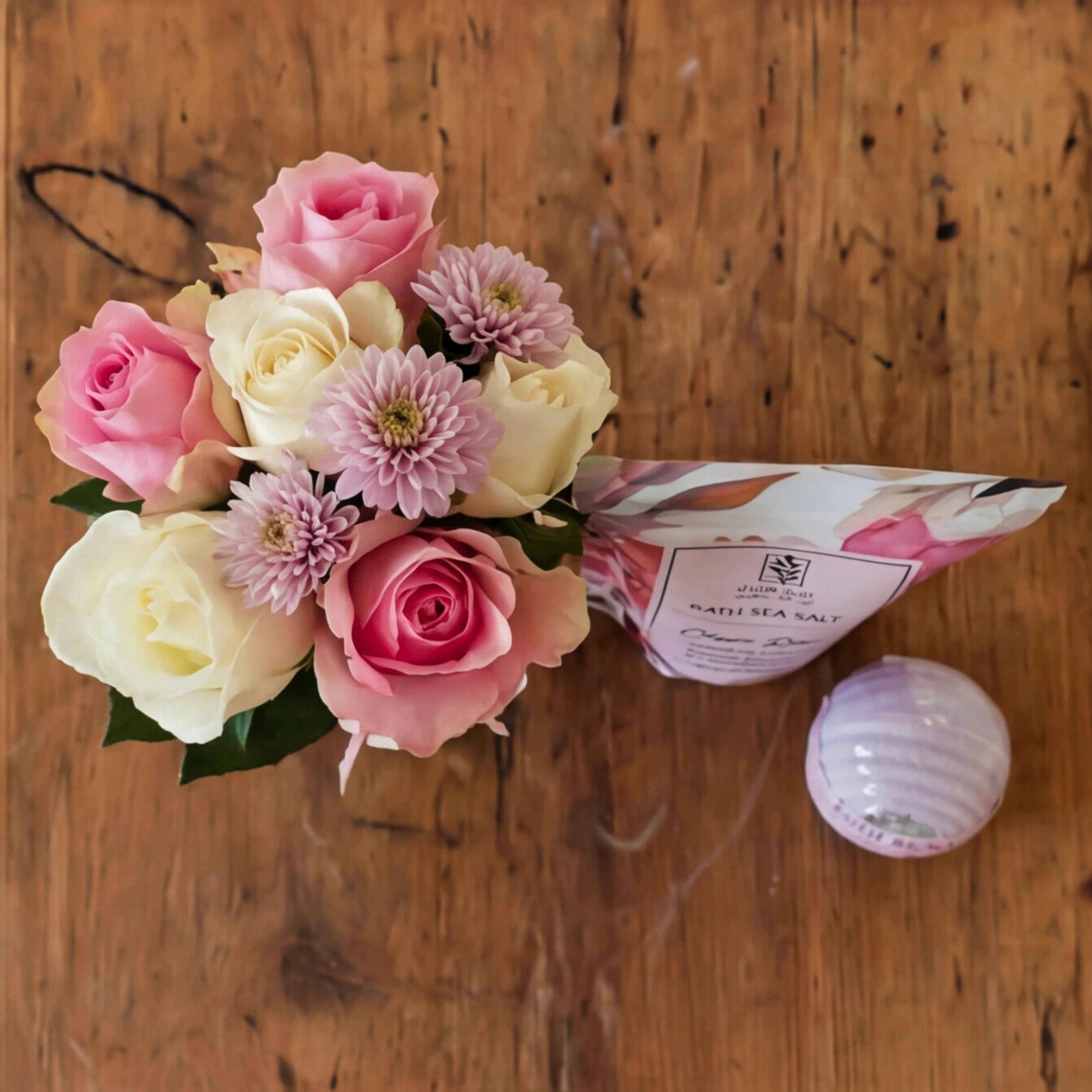 Top-down view of the Rose & Repose set, pink and cream roses in a vase beside bath salt and bath bomb