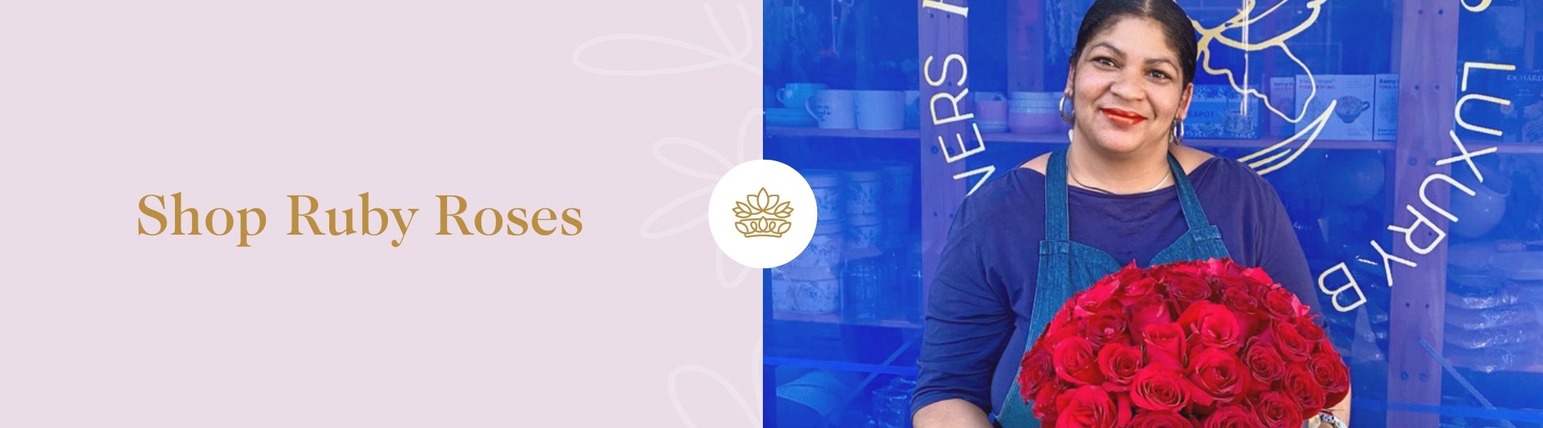 Woman smiling in blue apron holding lush ruby red rose bouquet in front of shop with “Shop Ruby Roses” – Fabulous Flowers and Gifts.