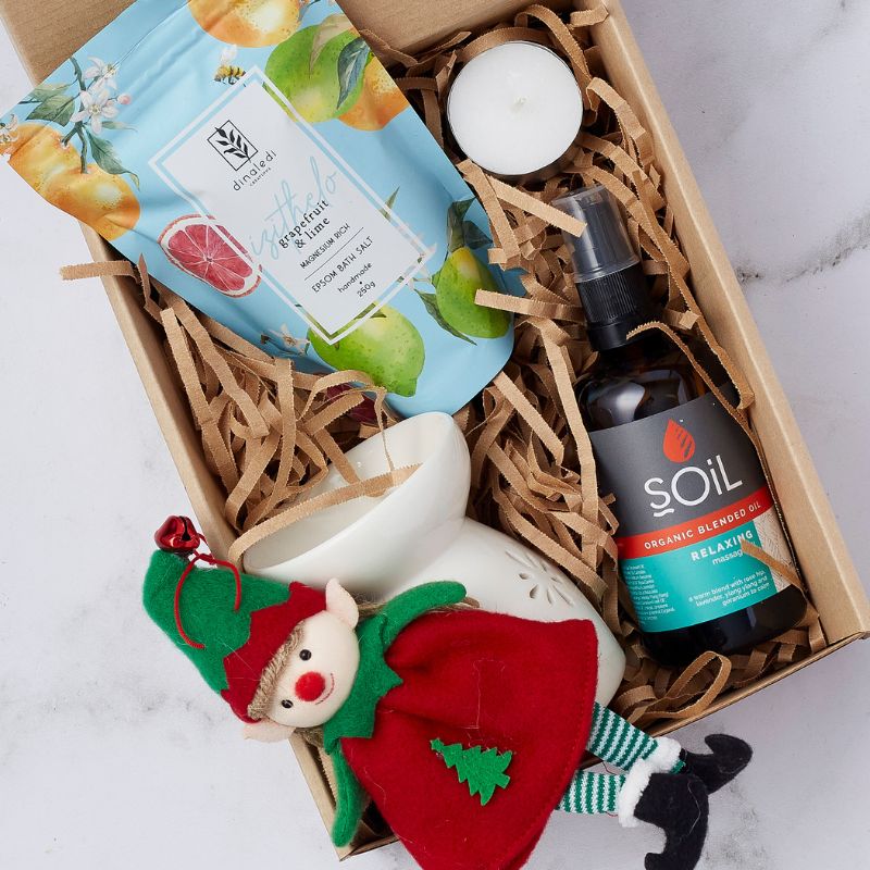 Gift box with ceramic oil burner, grapefruit and lime bath salts, organic relaxing massage oil, and a holiday elf plush toy.