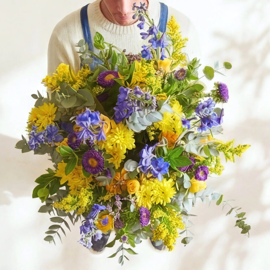 Spring Personified bouquet held close, yellow chrysanthemums, blue delphinium, purple asters and eucalyptus.