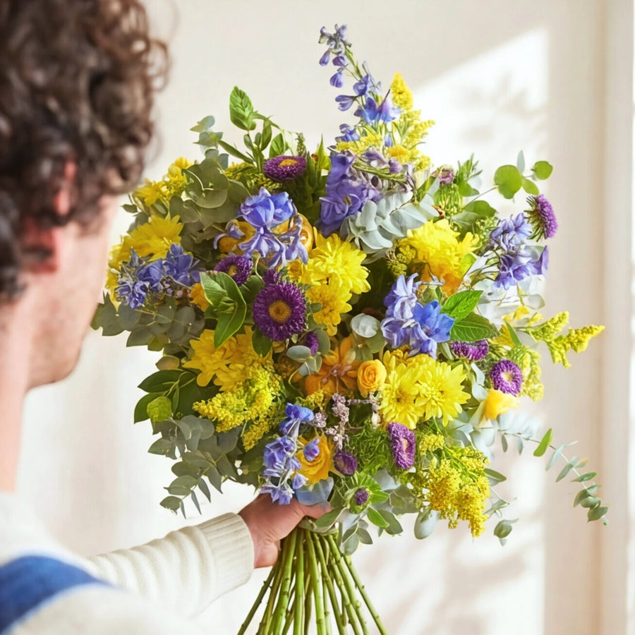 The Spring Personified spring bouquet in bright light, yellow chrysanthemums, blue delphinium and purple asters.