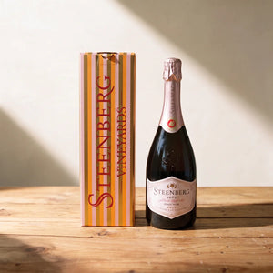 Bottle of Steenberg 1682 Pinot Noir Brut sparkling wine beside its striped gift box on a pine table, Fabulous Flowers South Africa