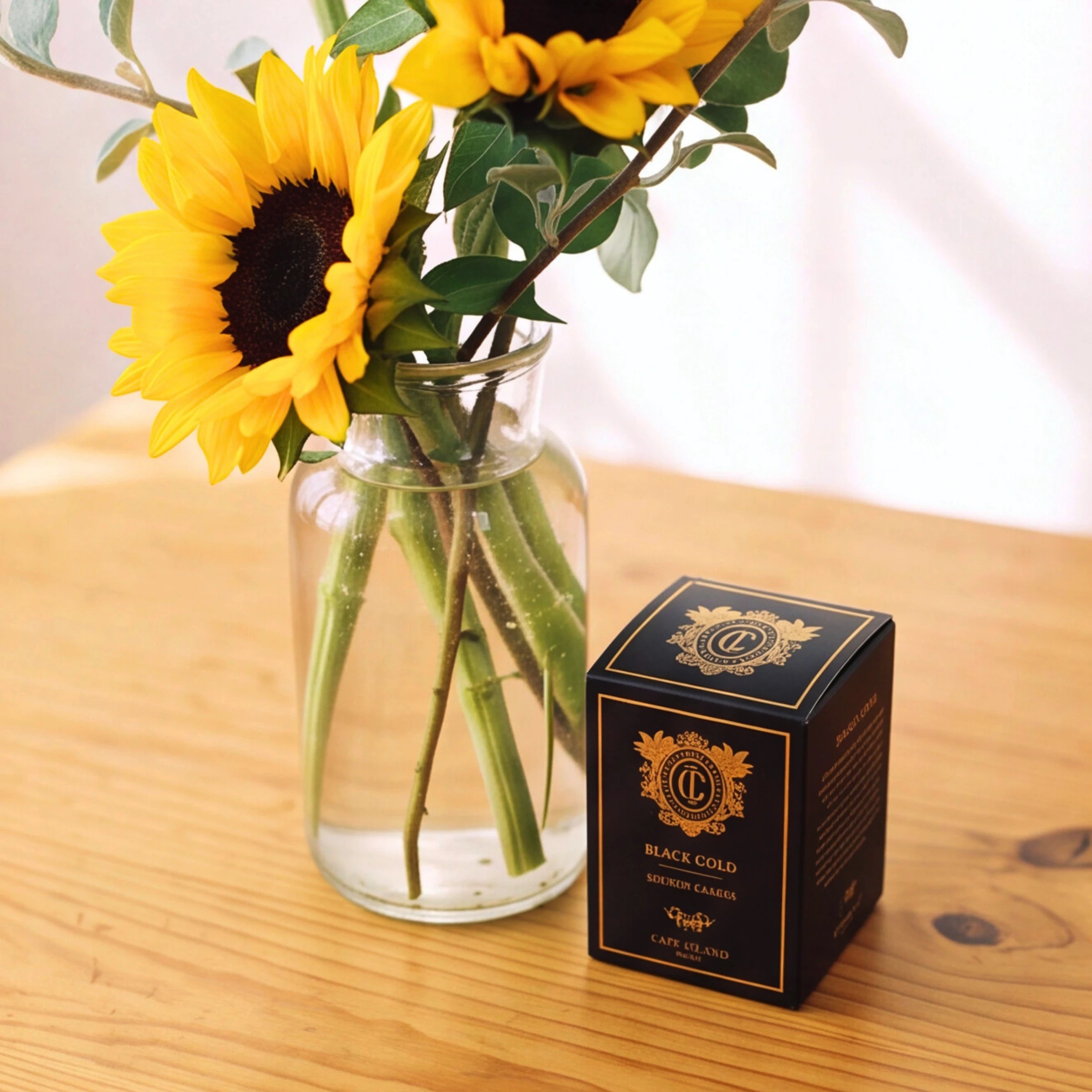 A black and gold box of 'Black Gold' Magic Cards by 'The Art of War' sits on a wooden table next to a glass vase filled with sunflowers.