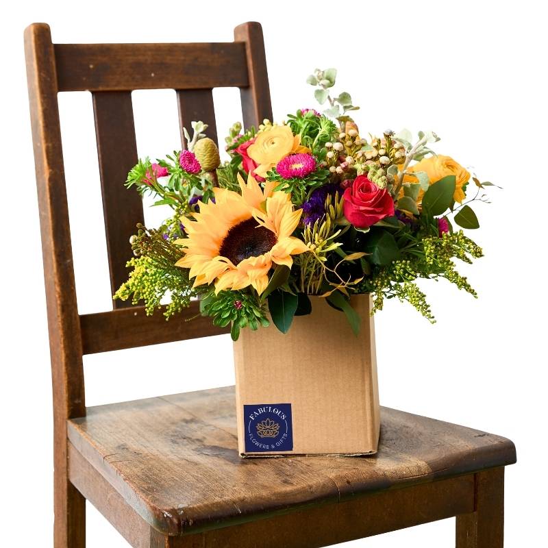 Sunflower Posy in kraft posy box on wooden chair — sunflower with bright seasonal blooms and lush greenery