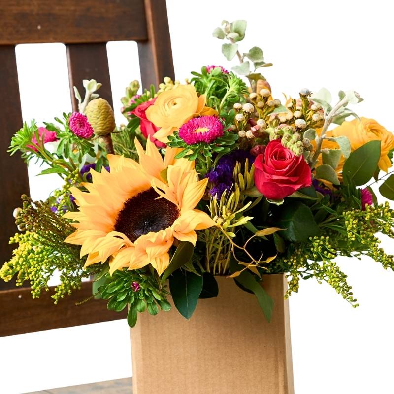 Sunflower Posy close-up — sunflower, red rose, yellow ranunculus and mixed seasonal flowers in a kraft posy box