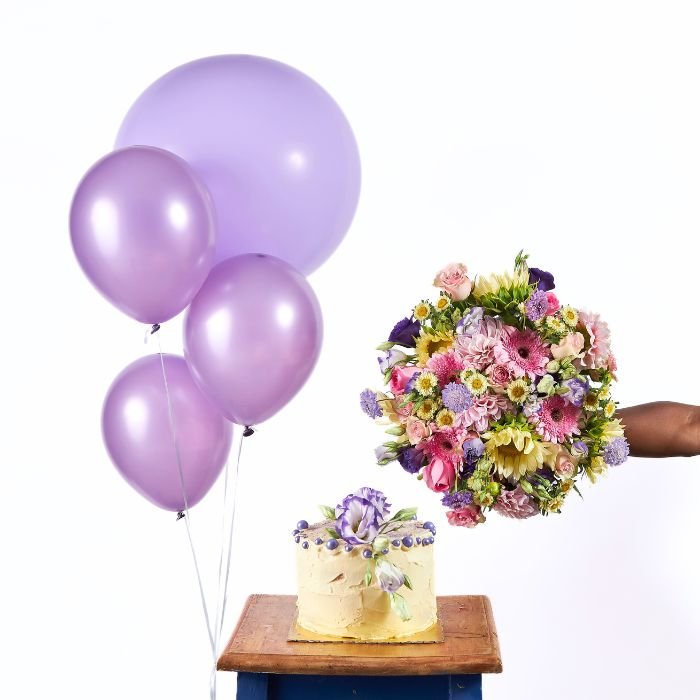 Sweet Celebration set with vibrant pink balloons, a colourful floral bouquet, and a buttercream cake topped with flowers, presented on a wooden stool.