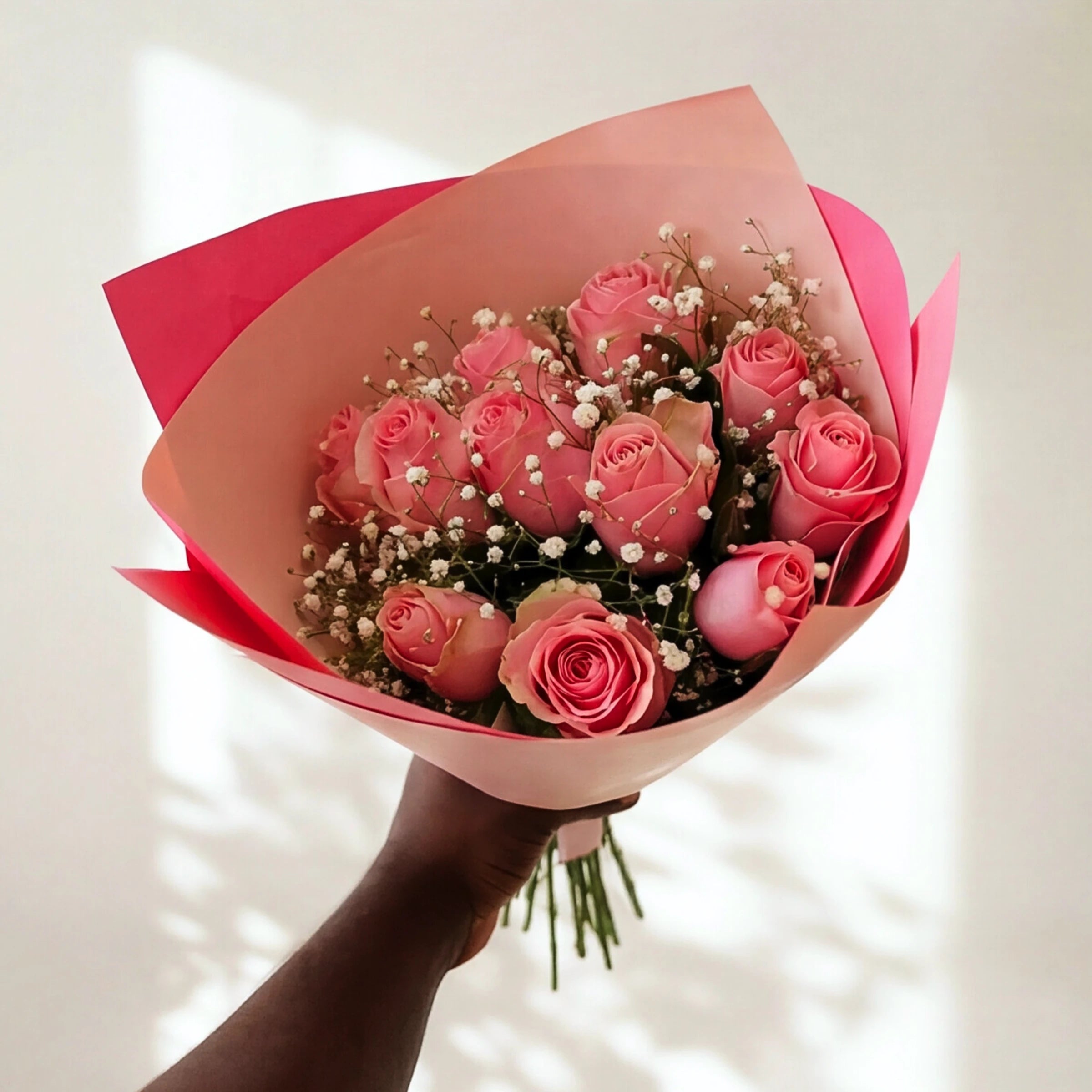 Sweet Talk soft pink roses with baby's breath in pink wrap, held in the sunlight