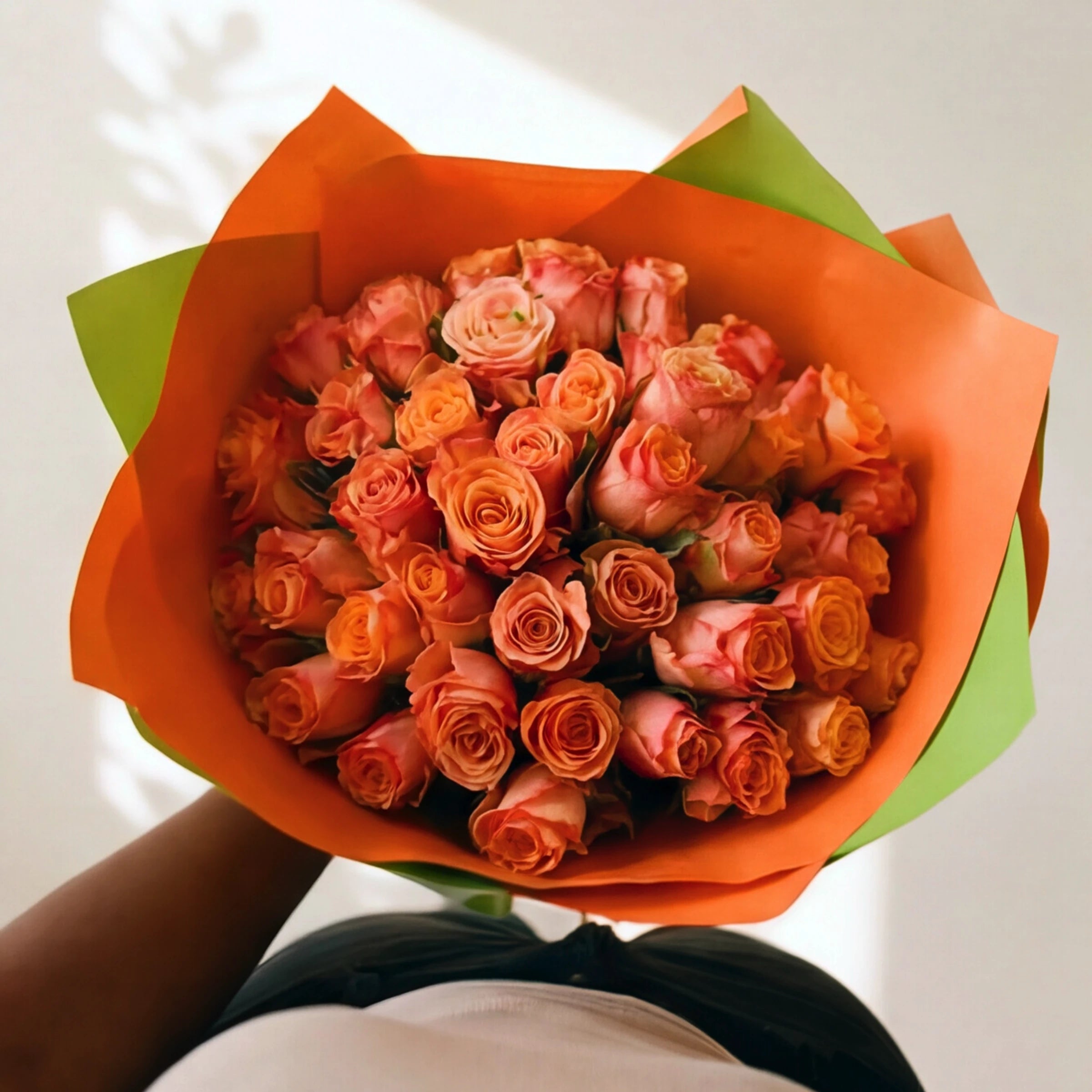 Top-down view of 50 orange roses in an orange and lime wrap, warm tangerine and coral tones.
