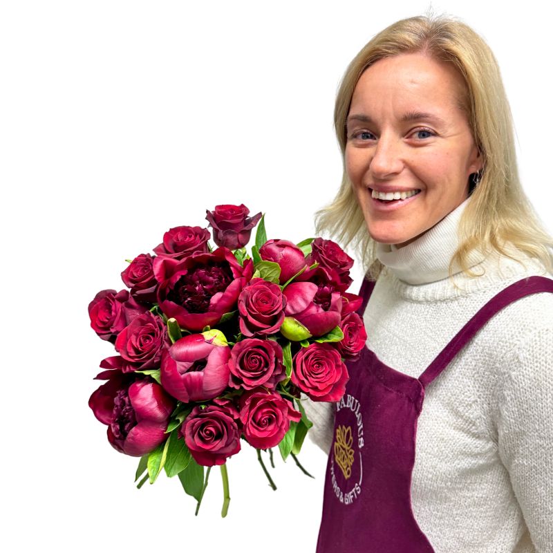 The Bloom Between Us bouquet with deep red peonies and red roses held by florist from Fabulous Flowers and Gifts.