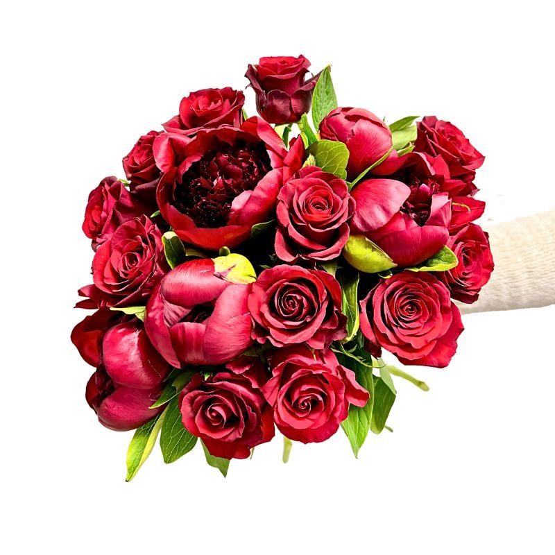 The Bloom Between Us bouquet of vibrant red roses and peonies displayed on a white background at Fabulous Flowers and Gifts.