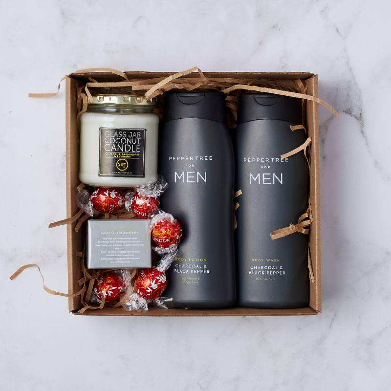 The Gentleman’s Essentials Gift Box with Peppertree body wash and lotion, a glass jar coconut candle, and Lindt chocolates.