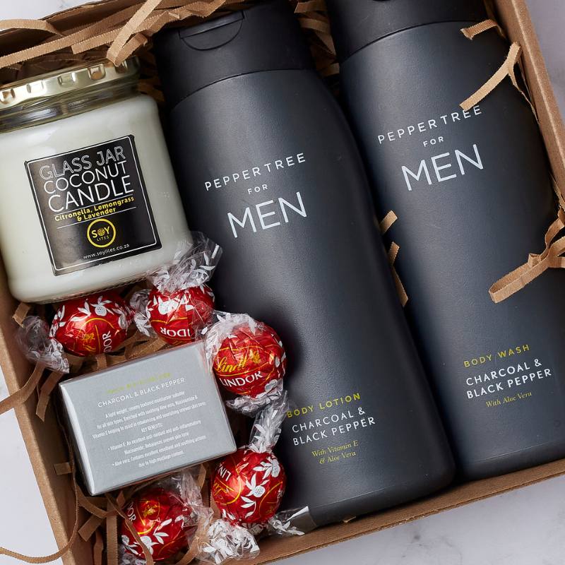 Close-up of The Gentleman’s Essentials Gift Box showing Peppertree for Men charcoal body wash and lotion, coconut candle, and chocolates.