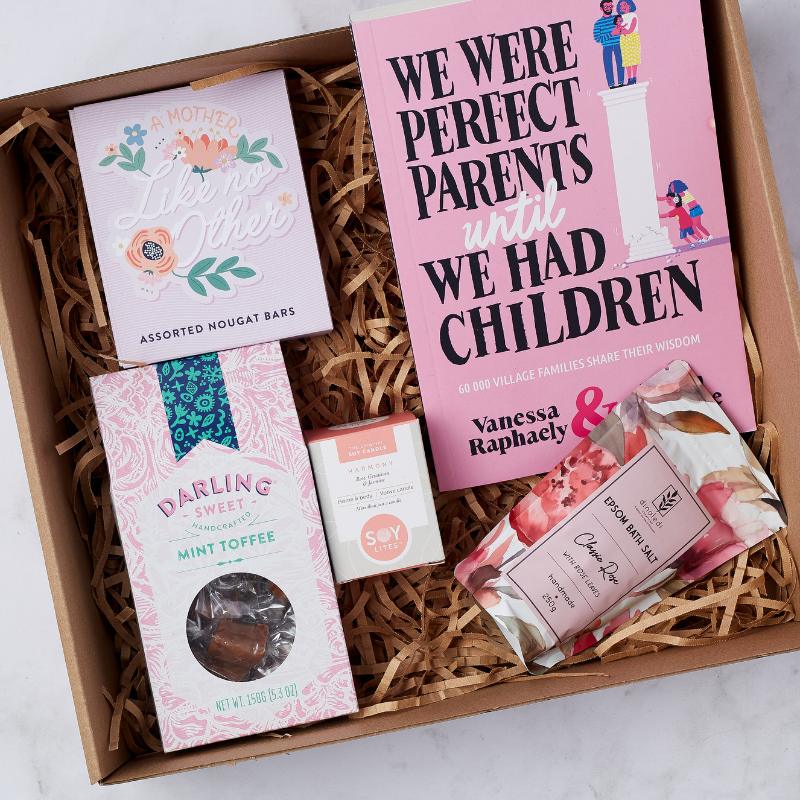 Close-up of The Perfect Parent Pamper Gift Box featuring a parenting book, assorted nougat bars, mint toffee, soy candle, and bath salts.