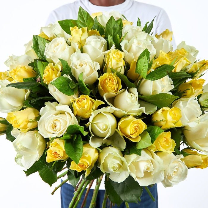 Close-up of a lush bouquet filled with yellow and white roses, presented by a joyful man, expressing sheer delight and brightness.