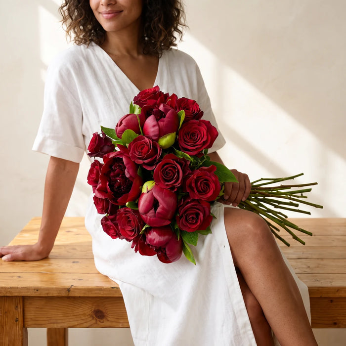 Woman seated with a red peony and red rose bouquet across her lap, same-day delivery Cape Town