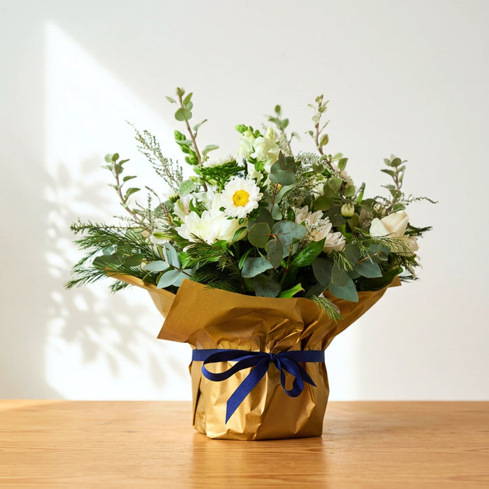 Tranquility white sympathy flowers, white blooms and eucalyptus in gold wrap tied with a navy ribbon.