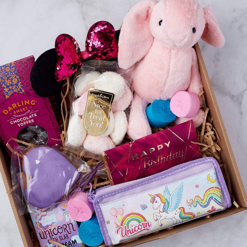 Close-up of Unicorn Dreams Gift Box featuring a pink plush bunny, bath bombs, chocolate treats, and unicorn pencil case.