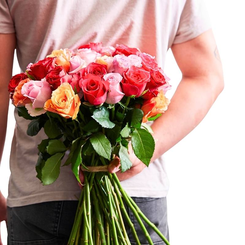 Hand holding a smaller vibrant mixed rose bouquet with red, lilac and orange blooms