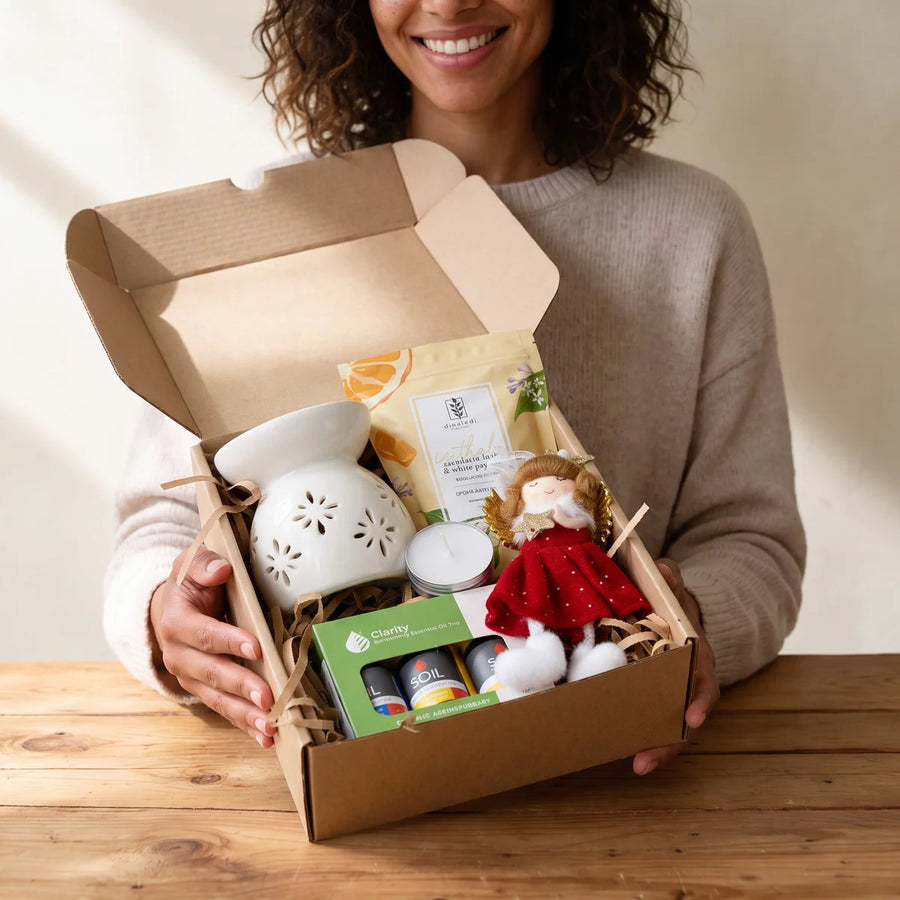 Smiling woman holding an open kraft box of bath salts, essential oils, an oil burner and an angel ornament, Fabulous Flowers South Africa